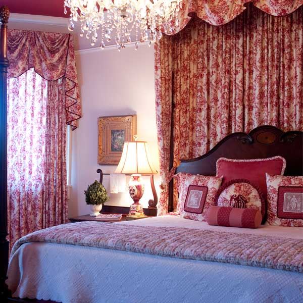 The Rose Room with a dark wood king bed, rose patterned drapes and a crystal chandelier